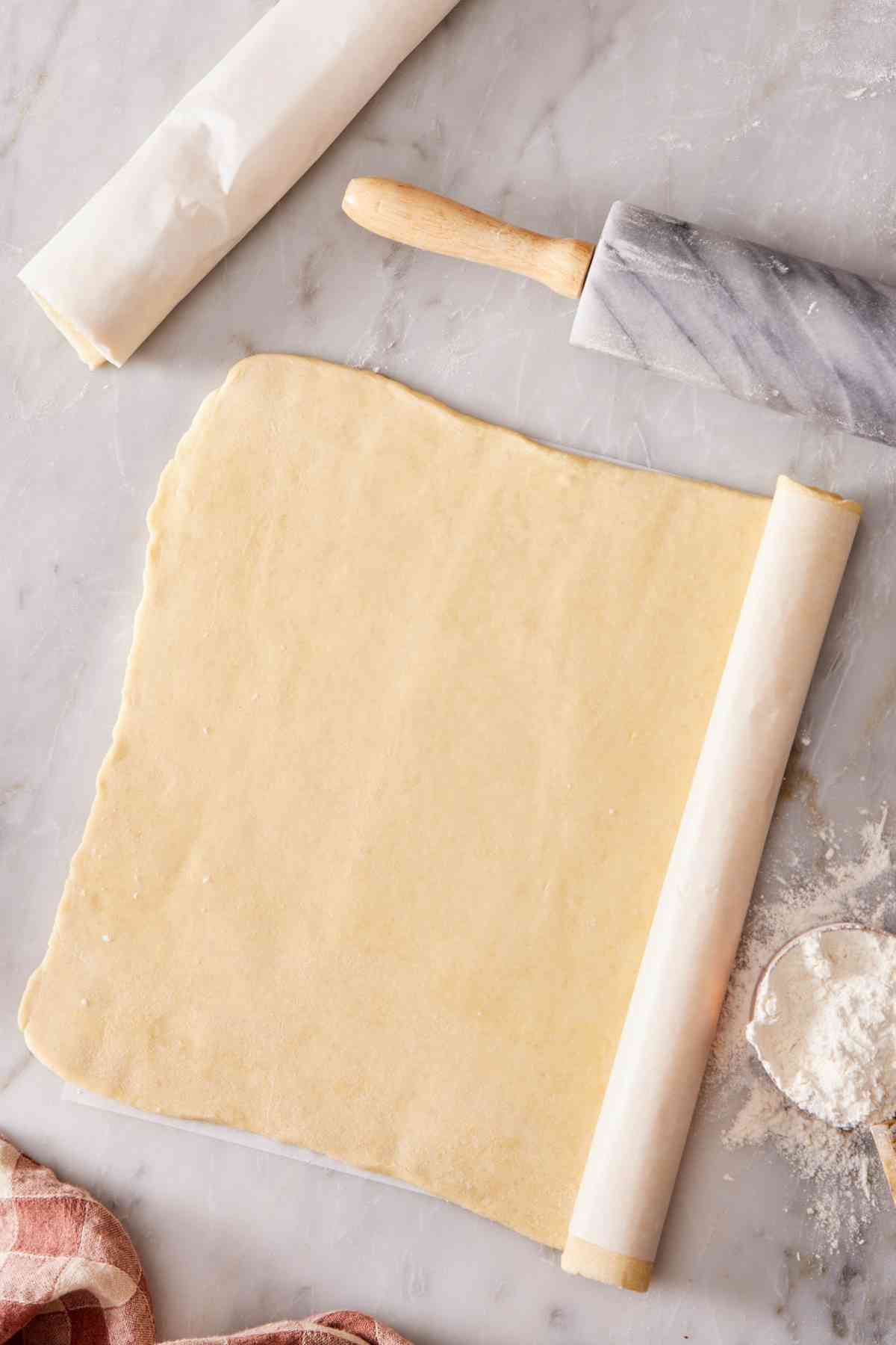 Overhead shot showing a sheet of puff pastry being rolled into a log with parchment paper for freezing.