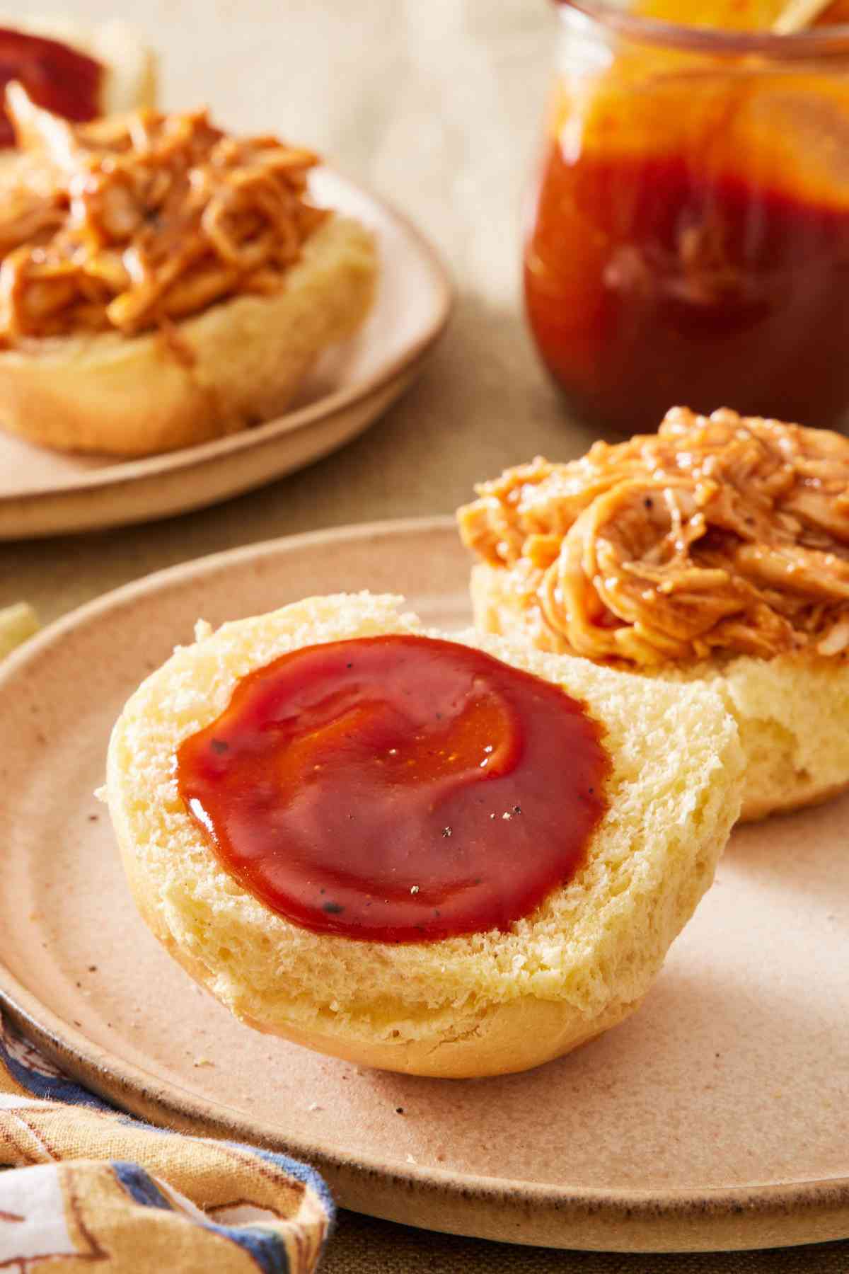 Sandwich with BBQ sauce spread onto one side of the bun and seasoned shredded meat on the other side.