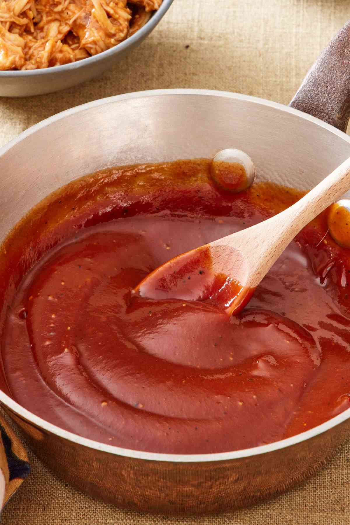 Barbecue sauce in a saucepan with a wooden spoon.