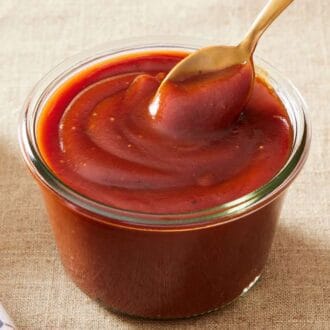 Close-up of a jar of homemade BBQ sauce recipe with a spoon dipped in.