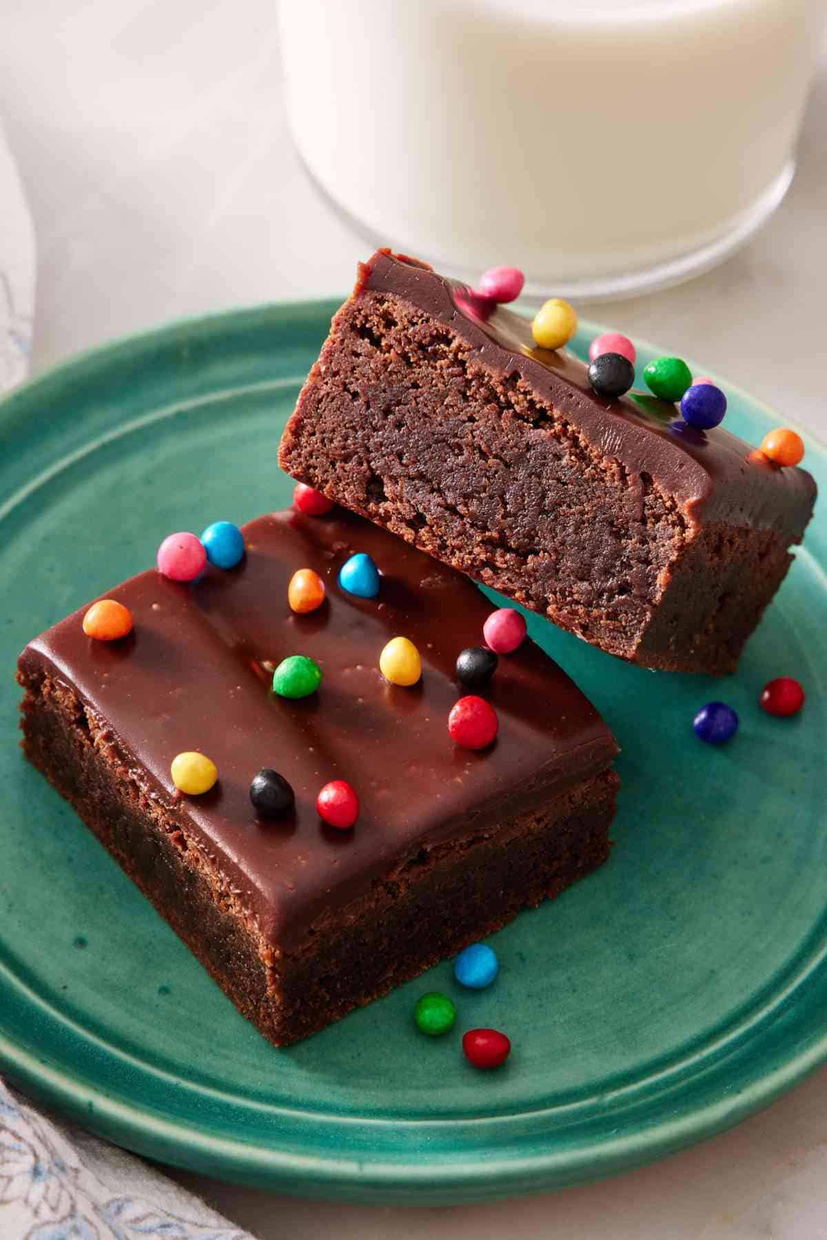 Two homemade cosmic brownies on a green plate with a glass of milk in the background.