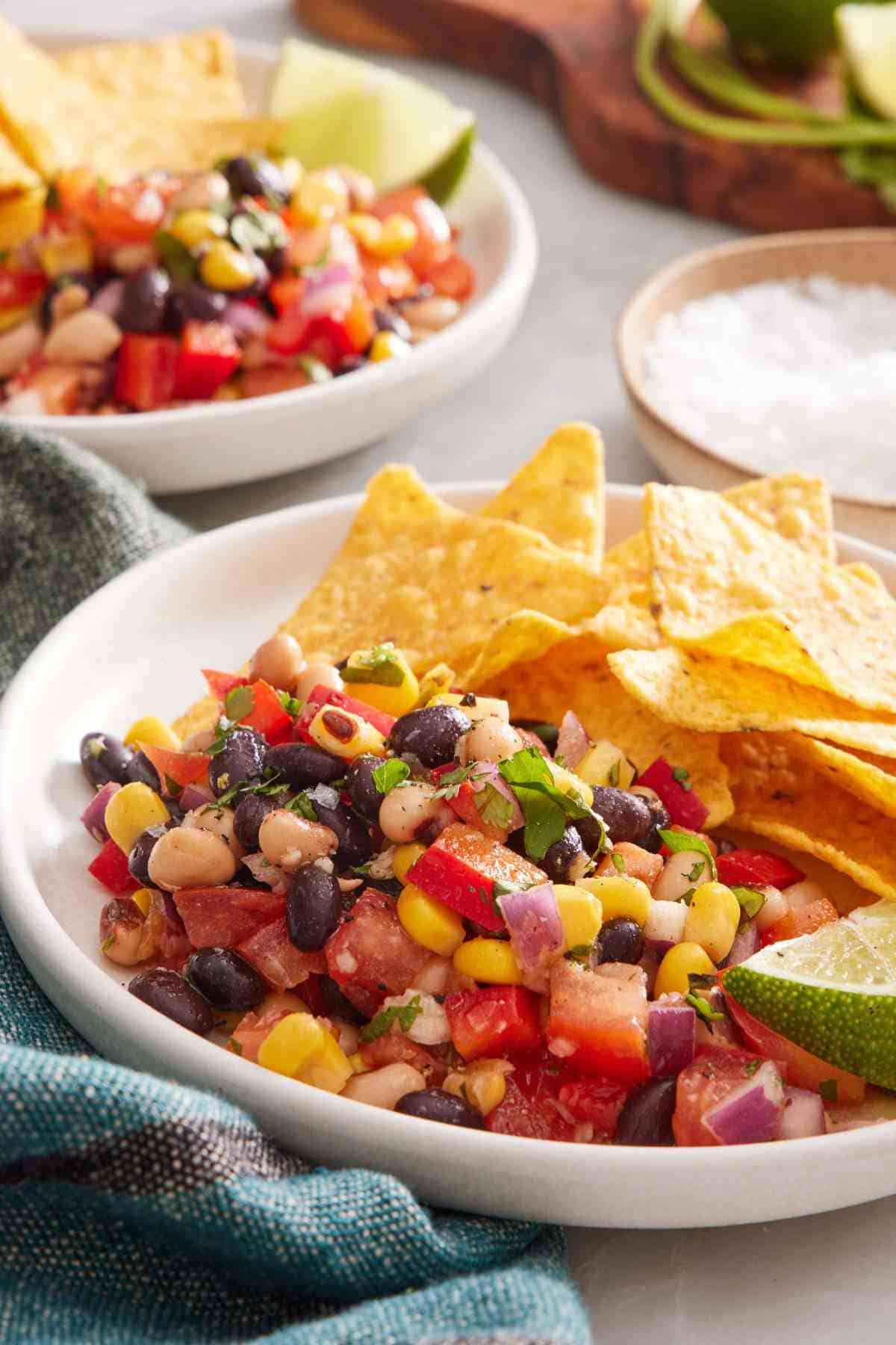 Close-up of a bowl of cowboy caviar recipe with chips and a lime wedge.