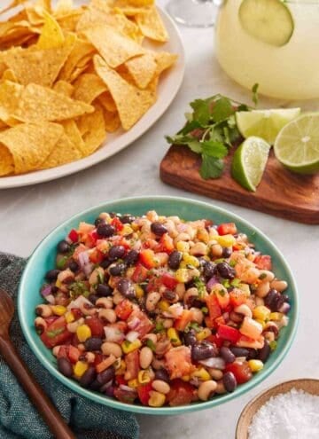 Cowboy caviar in a blue bowl with salt, chips, cilantro, and lime around it.