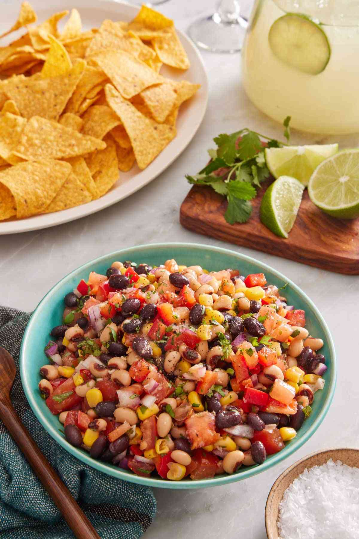 Cowboy caviar in a blue bowl with salt, chips, cilantro, and lime around it.