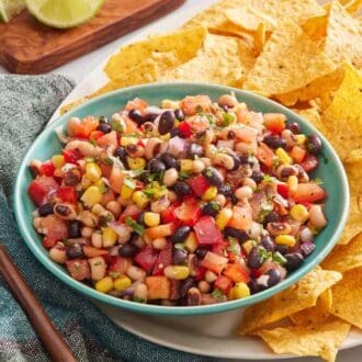 Texas caviar in a blue bowl set on a white platter with tortilla chips, and a wooden spoon off to the side.