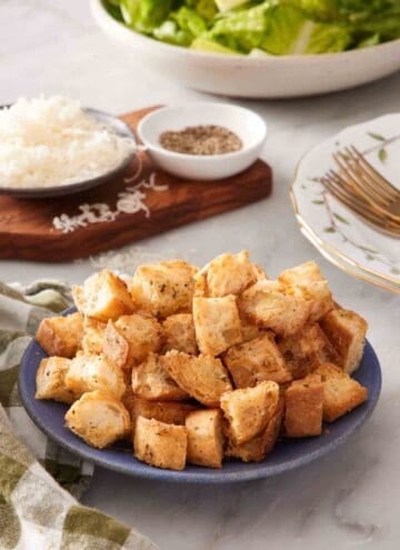 Croutons recipe in a small blue bowl with shredded cheese and black pepper in the background.