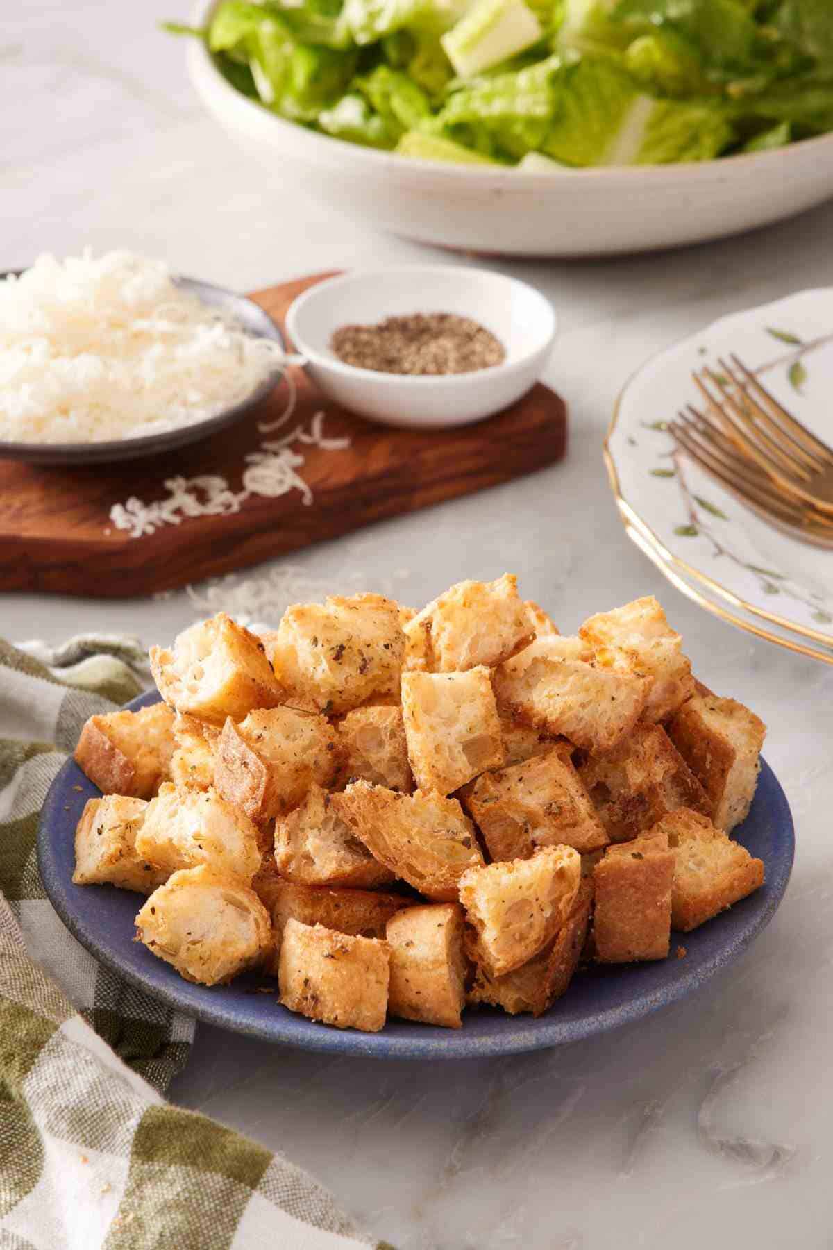 Croutons recipe in a small blue bowl with shredded cheese and black pepper in the background.