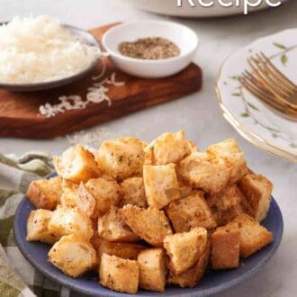 Pinterest graphic showing homemade croutons recipe in a small blue bowl with cheese and black pepper in the background.