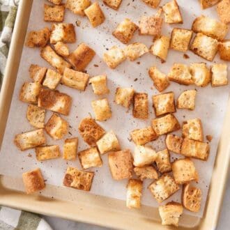 Overhead shot of croutons on a baking tray with a wooden spoon on the side.