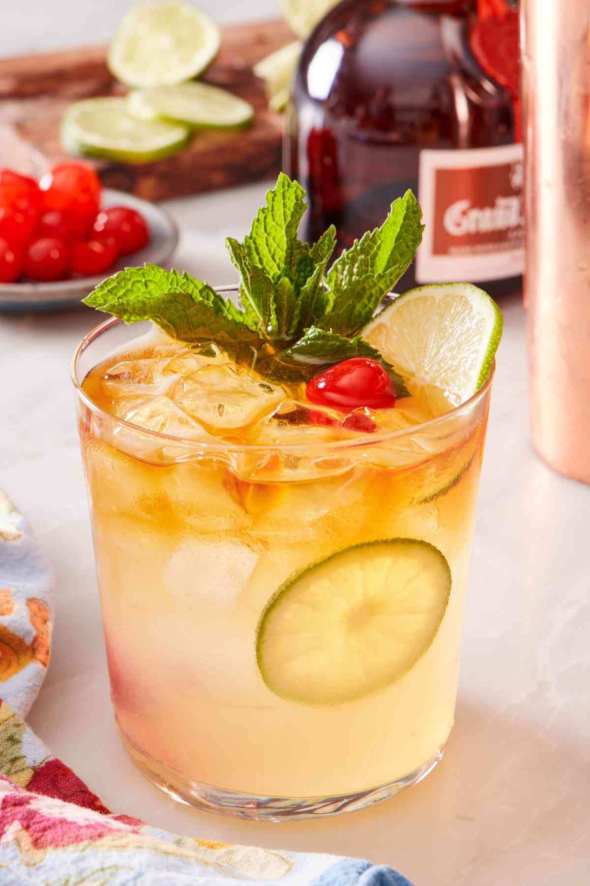 Close up of a mai tai drink garnished with fresh mint, lime wheels, and a Maraschino cherry.