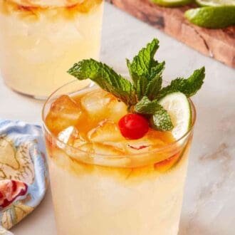 Pinterest graphic showing two mai tais with fresh garnishes, with a wooden board with more garnish in the background.