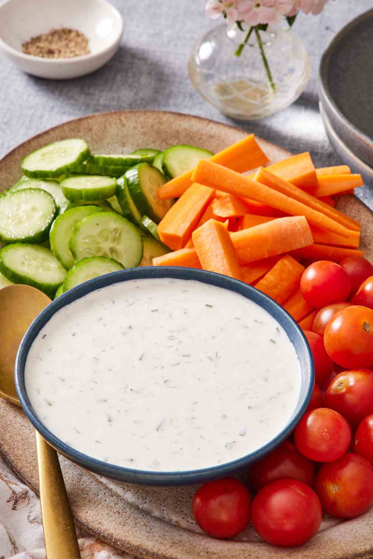 A bowl of ranch dressing on a platter with fresh vegetables.