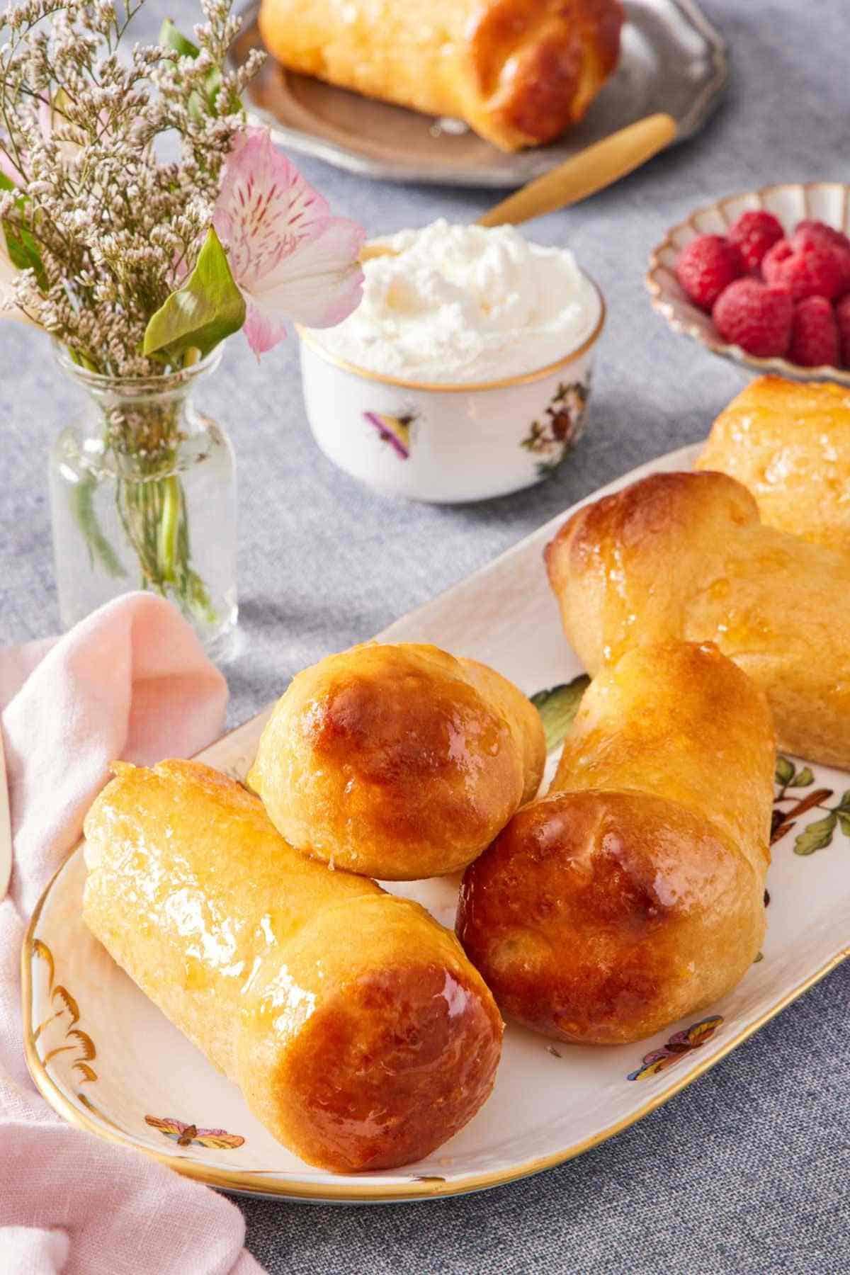Rum babas on a platter with some flowers, a container of whipped cream, and berries in the background.