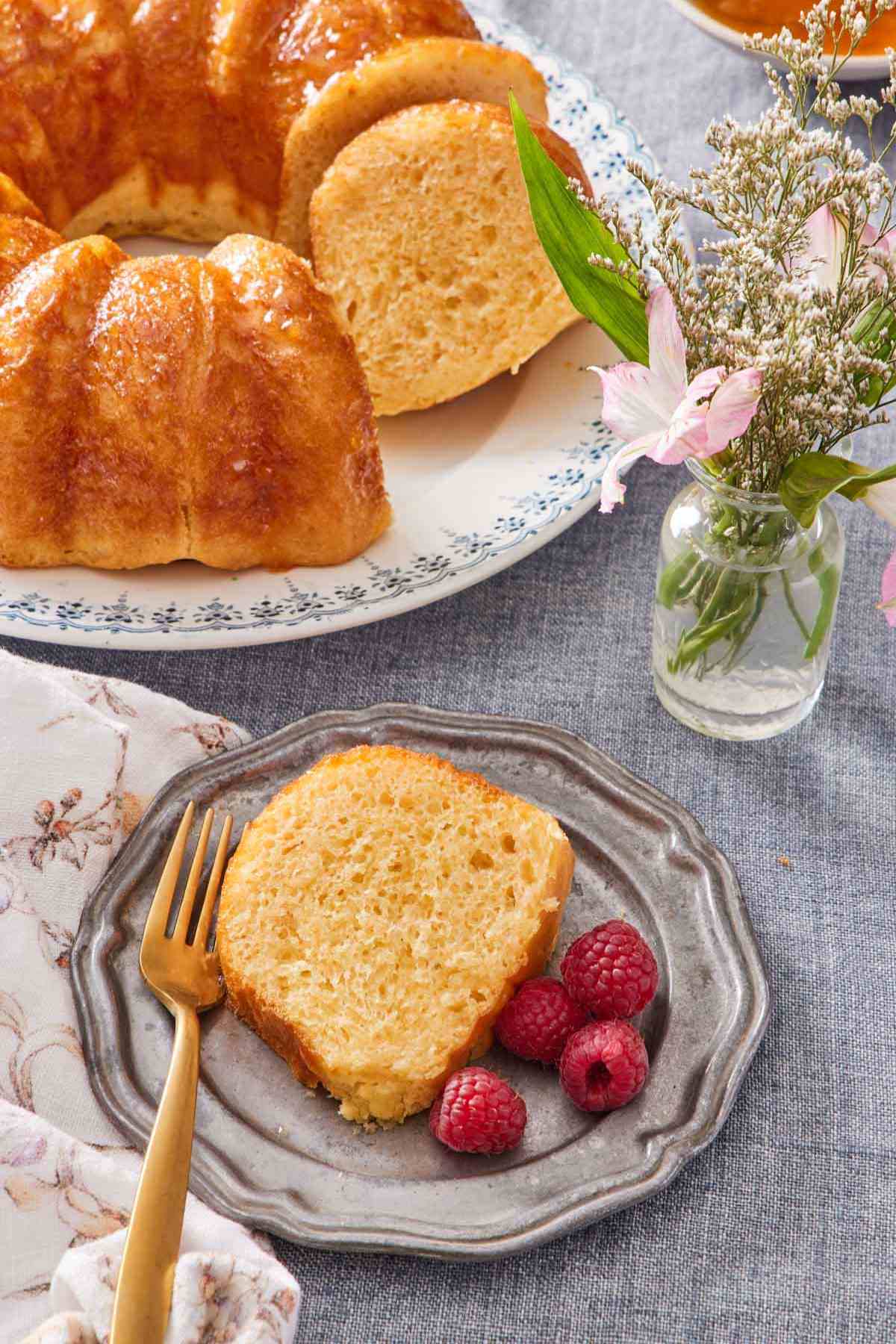 Slice of rum baba Bundt cake with berries on the side. The rest of the cake is on the side.