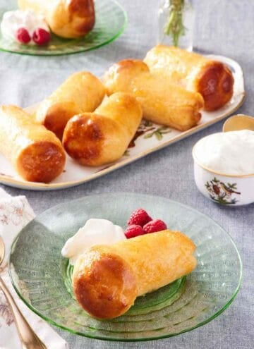 Baba au rhum on a plate with berries and whipped cream. Platter of rum babas in the background.