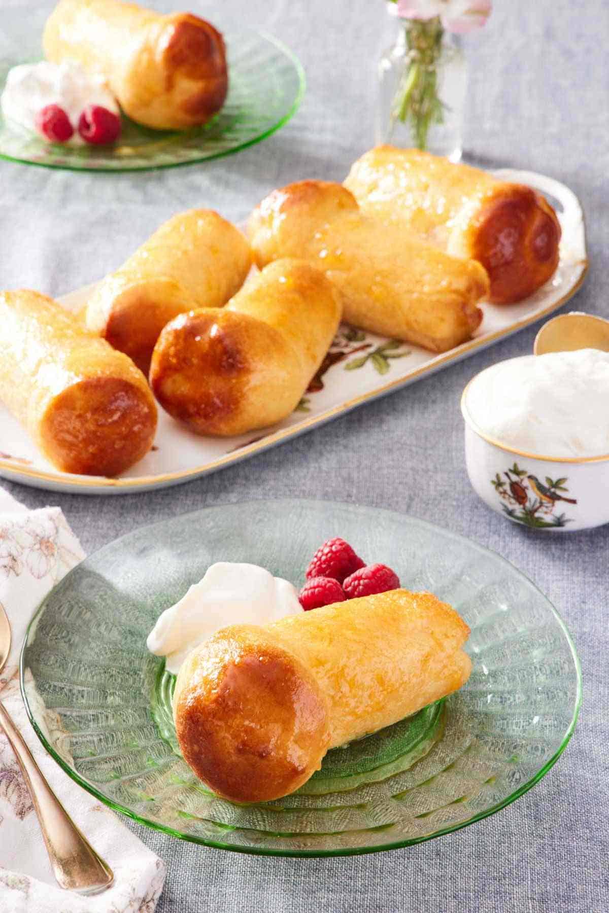 Baba au rhum on a plate with berries and whipped cream. Platter of rum babas in the background.