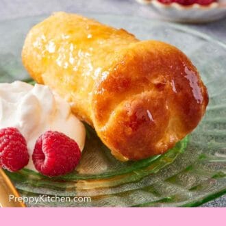 Pinterest graphic showing a close-up of a rum baba with raspberries and cream. A dish of raspberries in the background.
