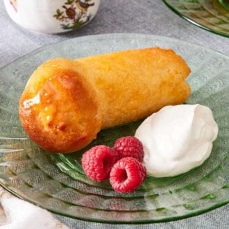 Rum baba on a plate with raspberries and cream on the side.