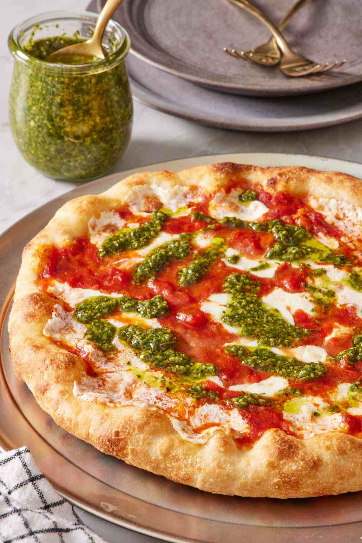 Close-up of a pizza with pizza sauce and pesto. A jar of pesto off to the side.
