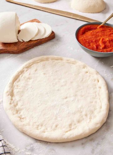 A rolled out sourdough pizza dough with pizza sauce and cheese on the side.