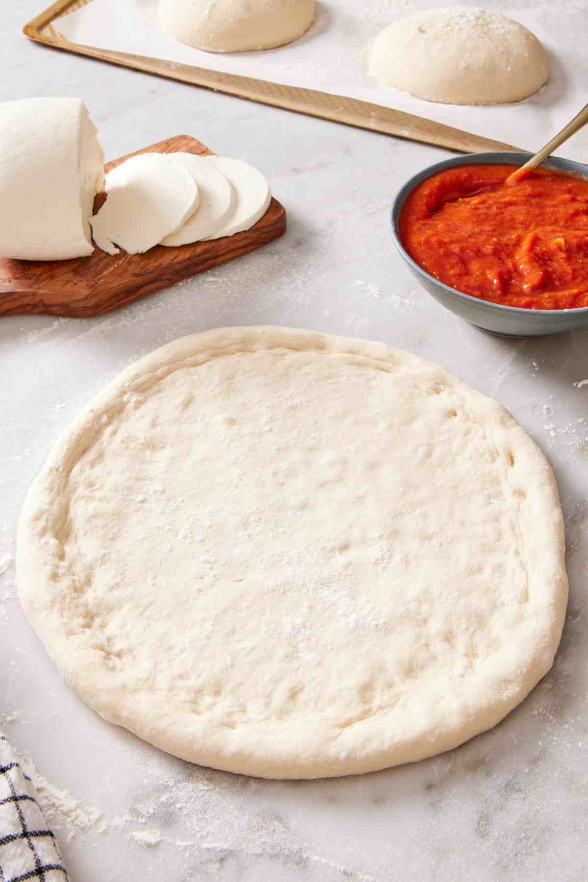 A rolled out sourdough pizza dough with pizza sauce and cheese on the side.