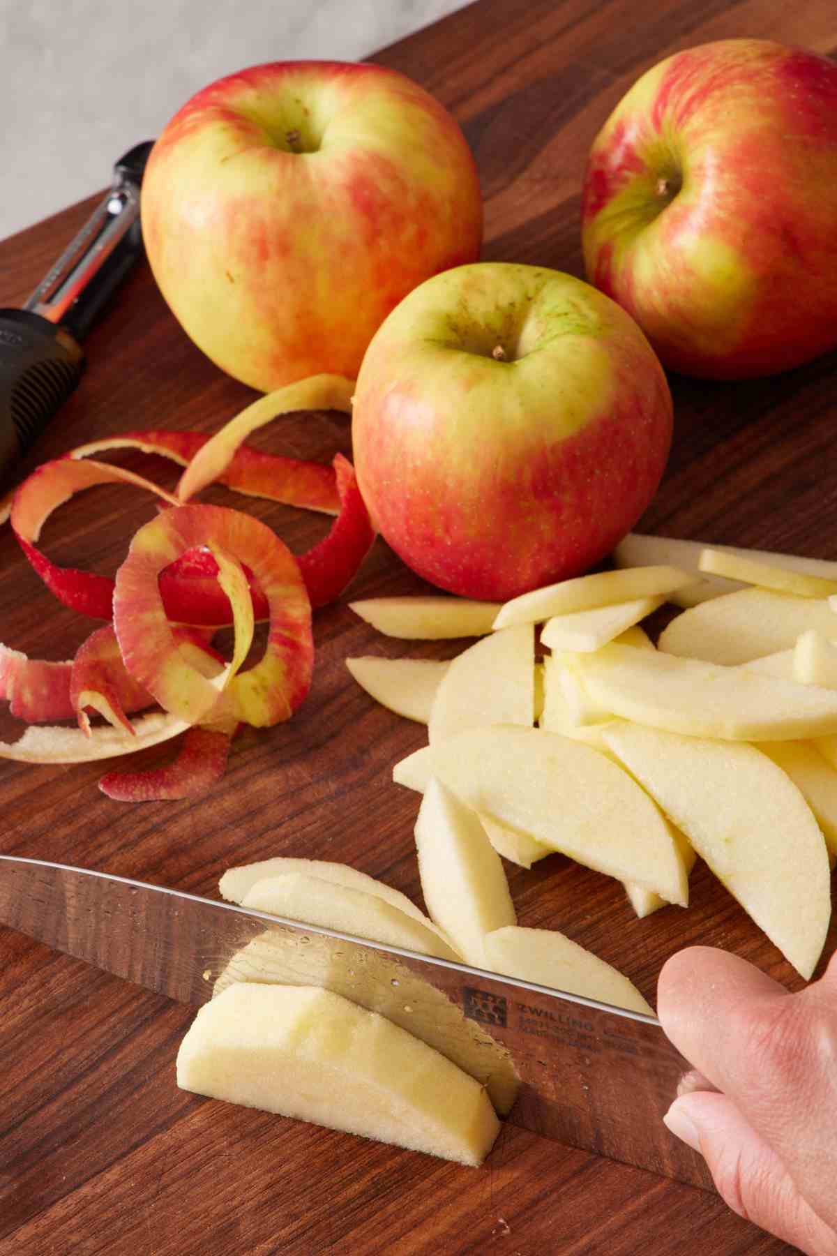 Apples sliced on a wooden cutting board with apple peels and whole apples on the board as well.