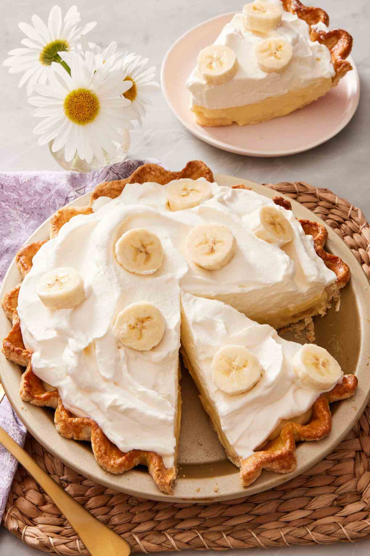 Banana cream pie with two slices cut out but one still in the pan. The other slice is on a small plate in the background.