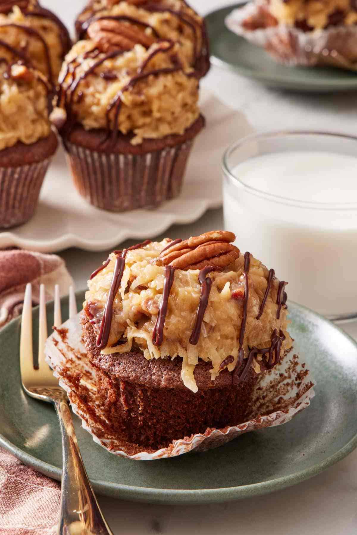 Easy German chocolate cupcake on a small plate with a fork next to a glass of milk. More cupcakes in the background.