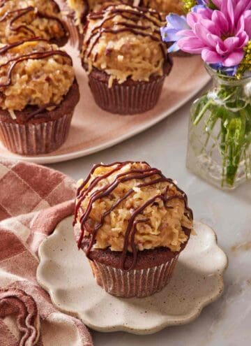 German chocolate cupcake on a small plate with a platter of cupcakes in the background.