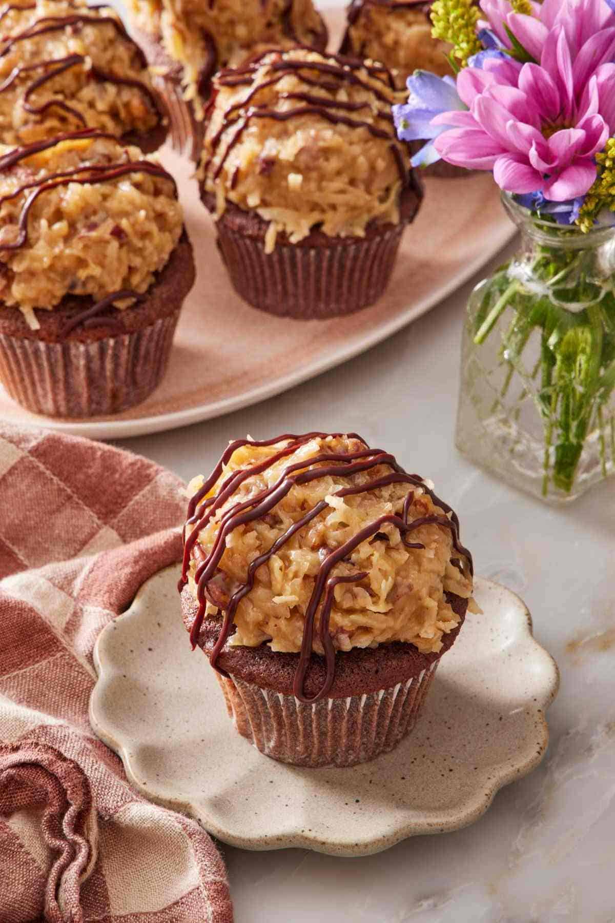 German chocolate cupcake on a small plate with a platter of cupcakes in the background.