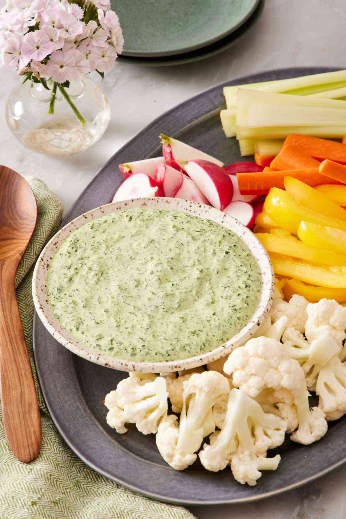 Green goddess dressing in a small bowl on a platter with various sliced vegetables.
