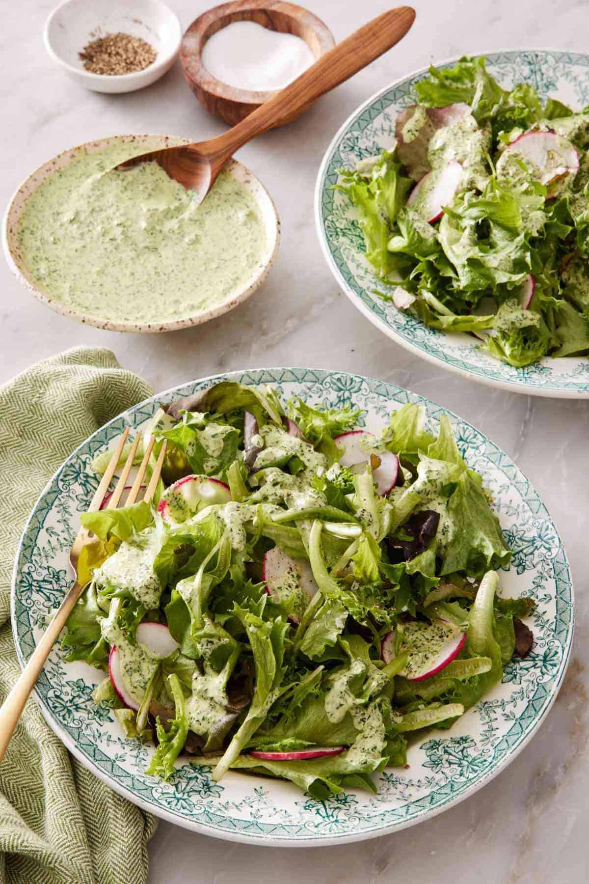 Two servings of salad in patterned plates with a small bowl of green goddess salad dressing in the background.