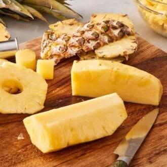 Pineapple rings and quartered pineapple on a wooden cutting board.