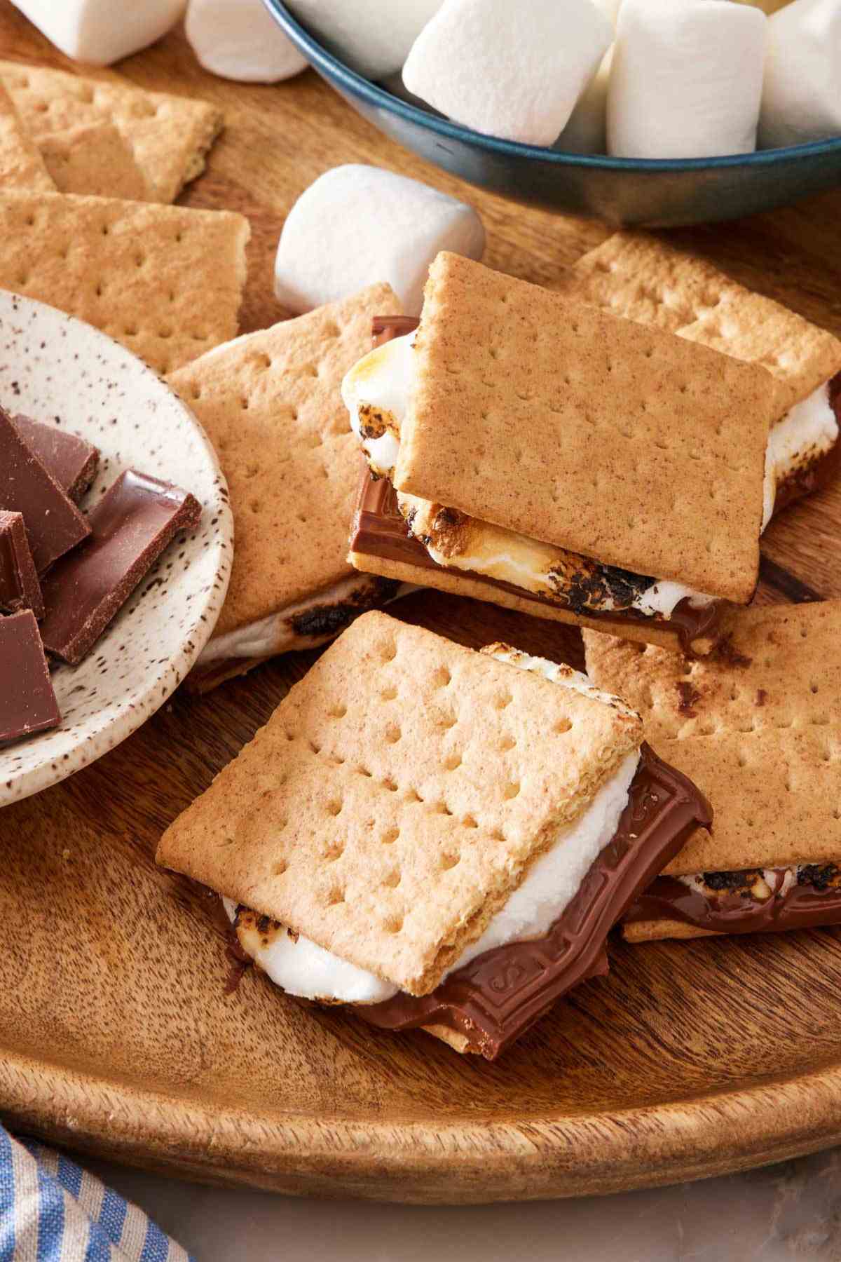 Wooden platter of s'mores recipe with a small dish of chocolate half in frame.