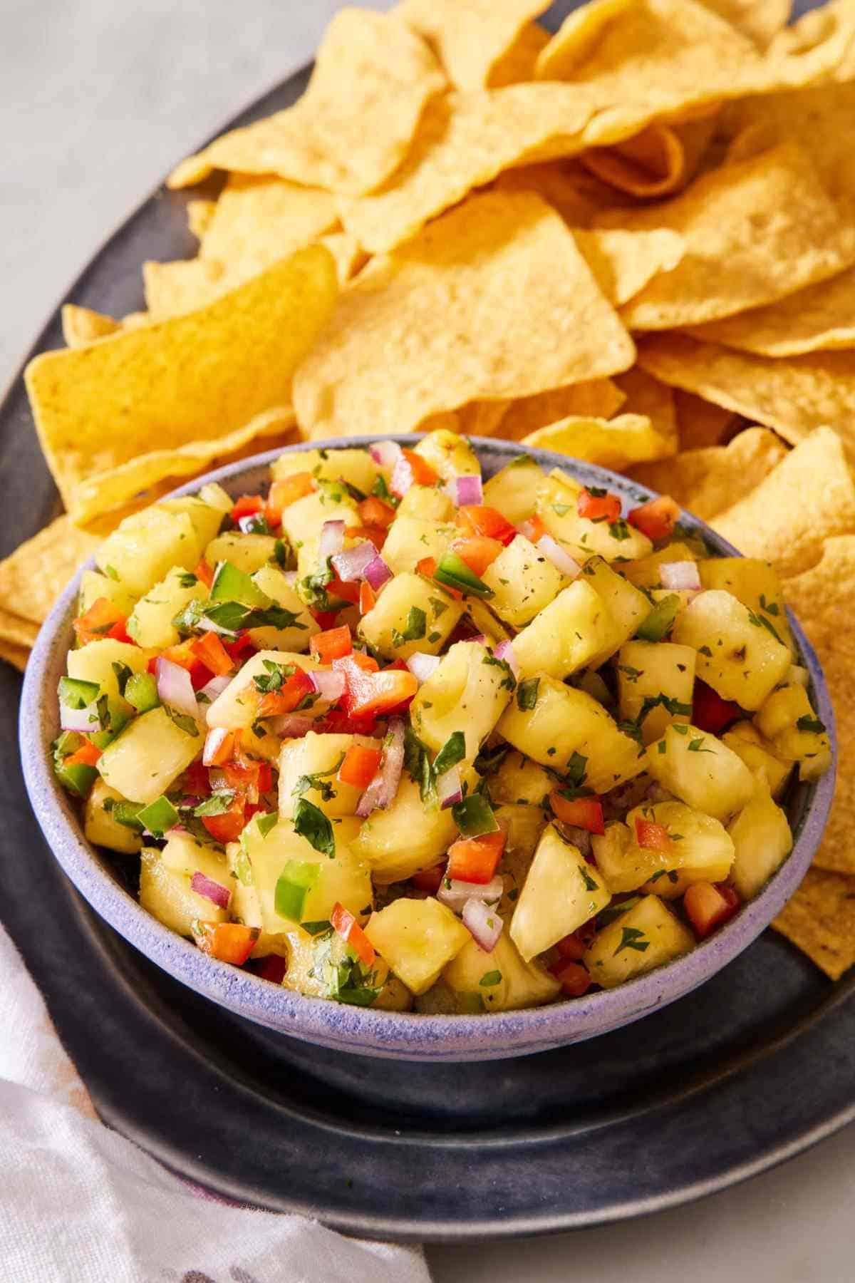 Pineapple salsa in a bowl set on a platter with tortilla chips.
