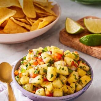 Pinterest graphic showing easy pineapple salsa in a bowl with a gold spoon next to it. Lime wedges and chips in the background.