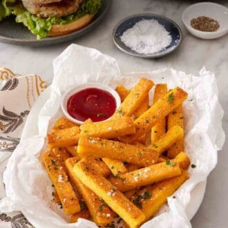 Pinterest graphic showing a dish of polenta fries with ketchup with a burger in the background.
