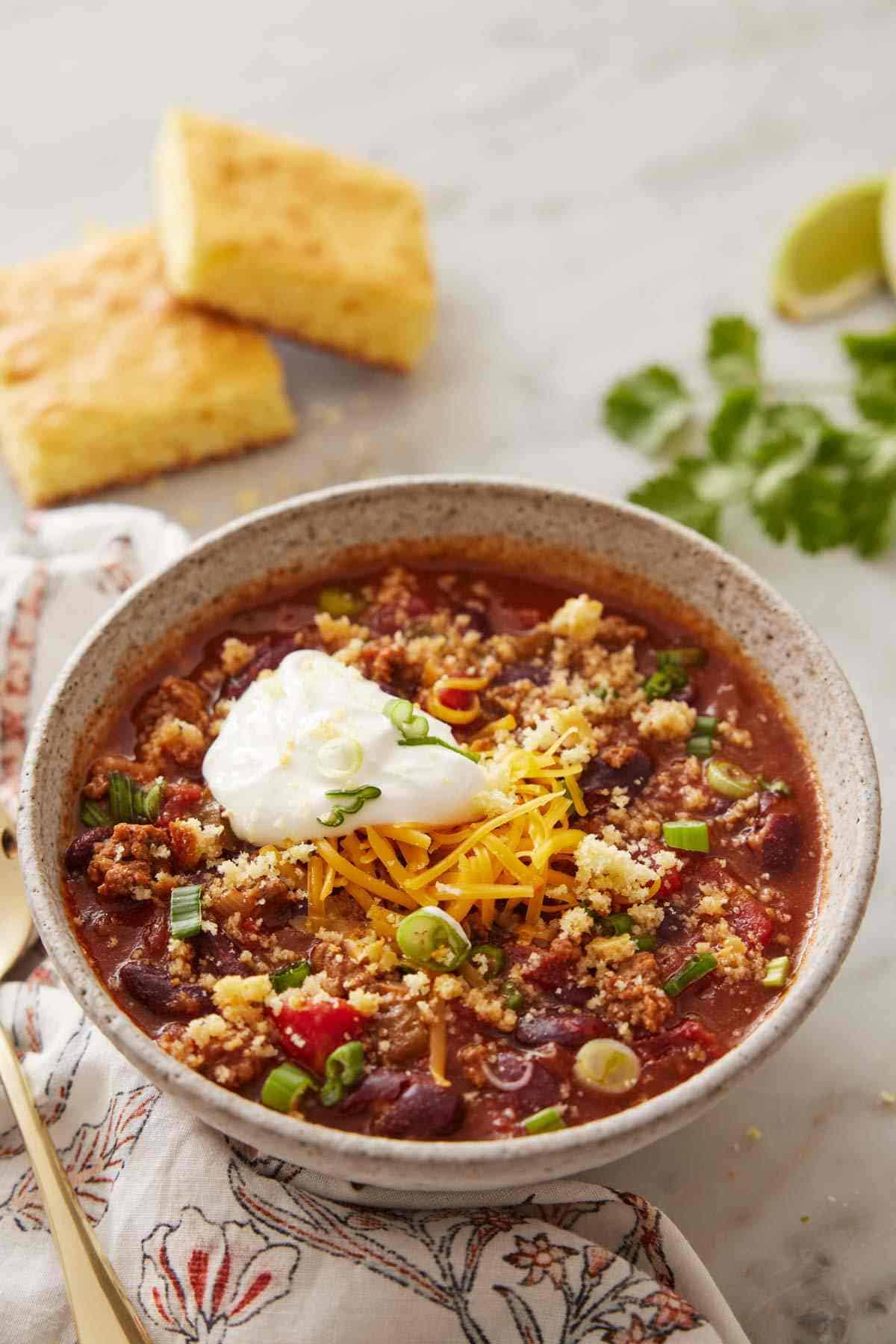 A bowl of slow cooker chili topped with sour cream, sliced green onion, and shredded cheese.