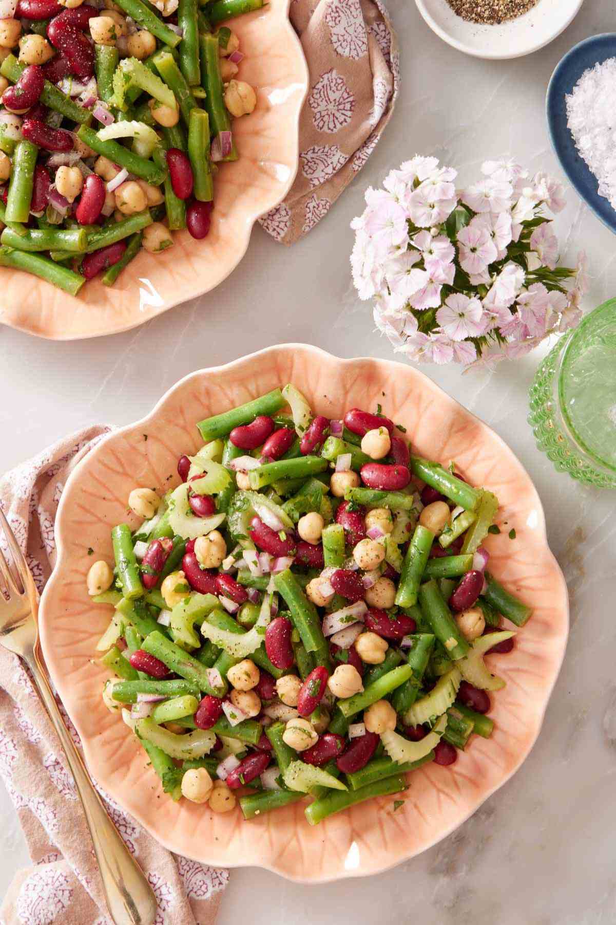 Overhead shot of a serving of easy bean salad recipe with a vase of flowers alongside. Another serving of salad is slightly out of frame.