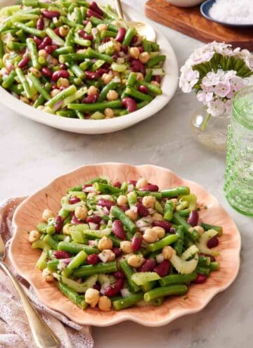 Easy bean salad recipe on a pink plate with the rest of the salad in a platter in the background.