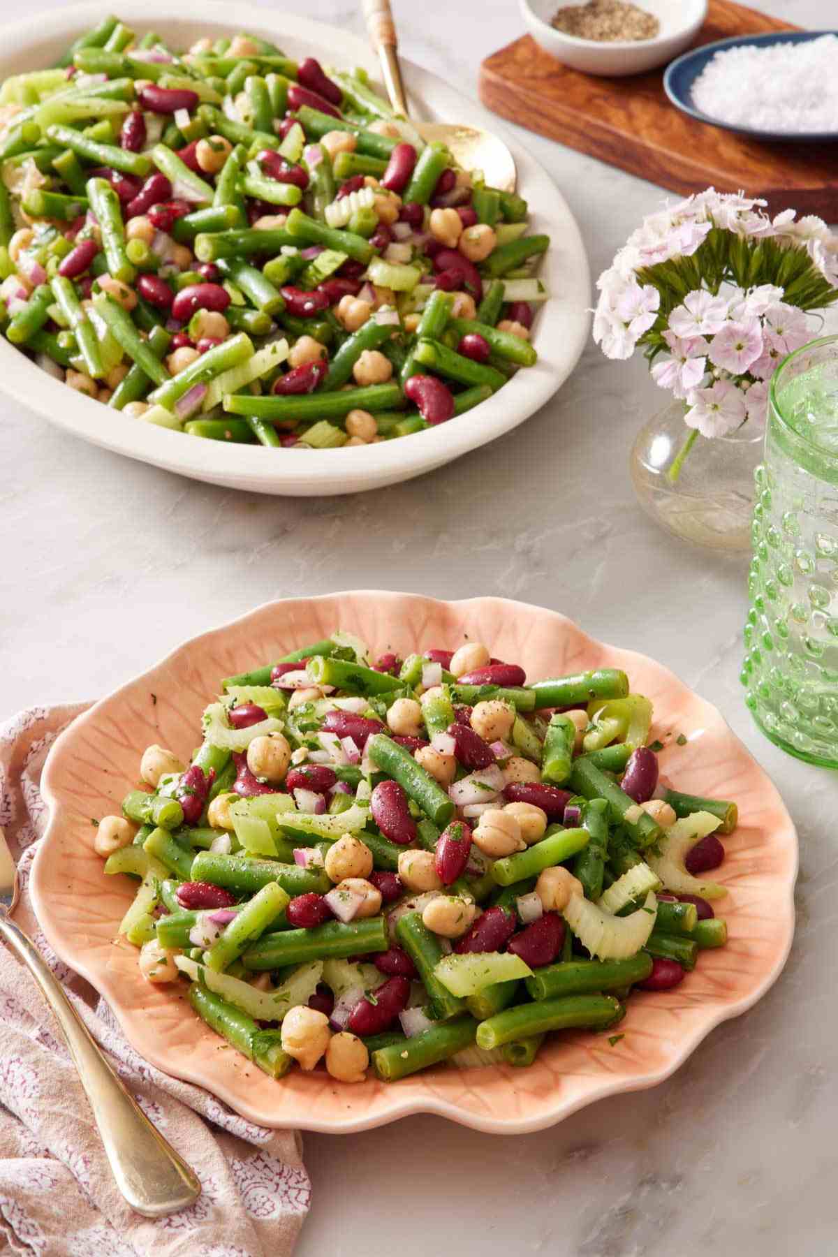 Easy bean salad recipe on a pink plate with the rest of the salad in a platter in the background.