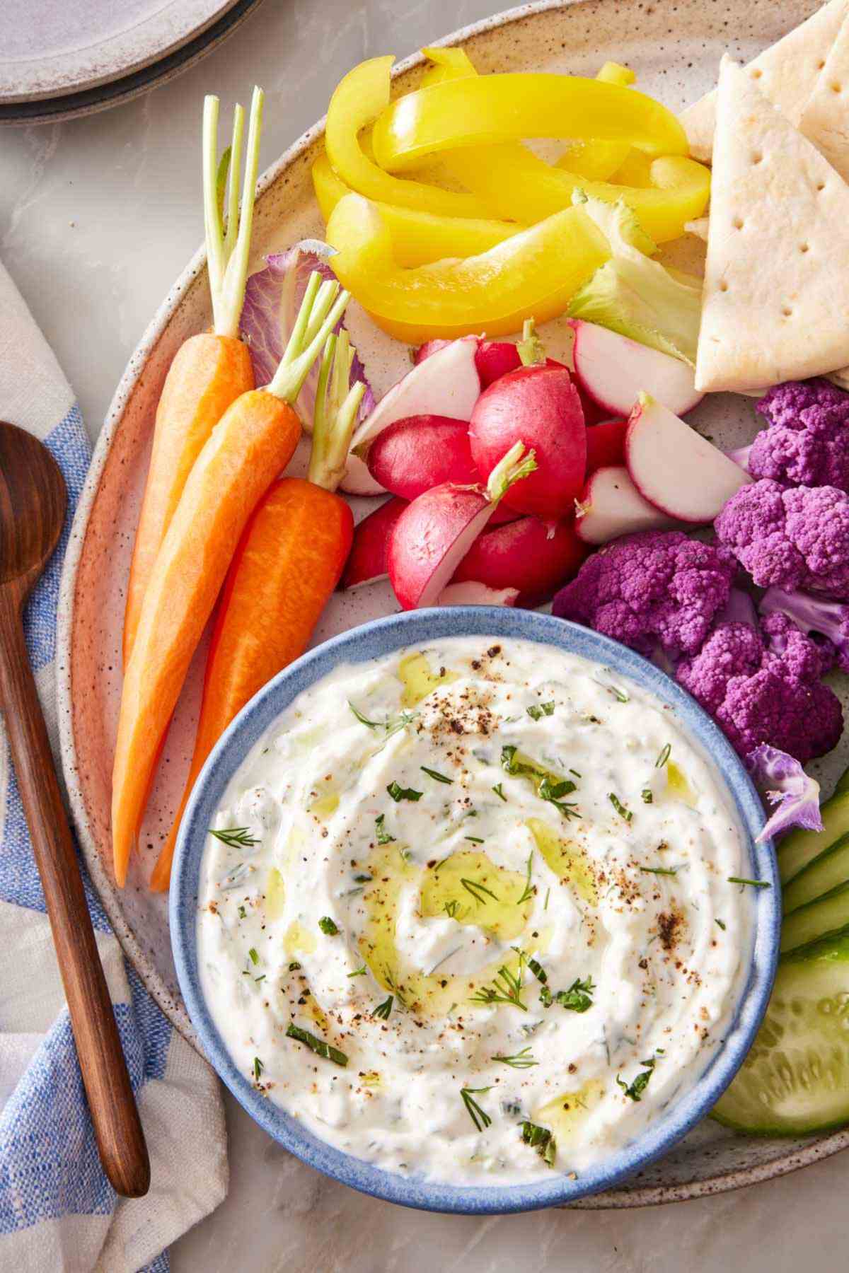 Homemade tzatziki in a bowl on a platter with fresh vegetables.
