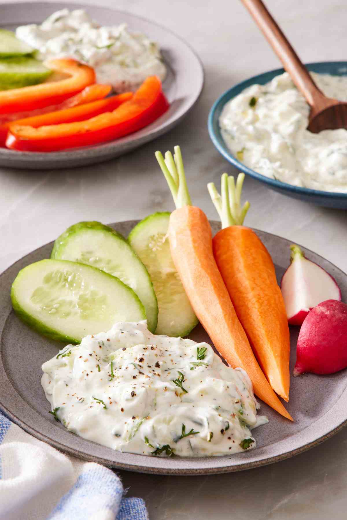 A serving of creamy tzatziki on a small plate with colorful veggies.