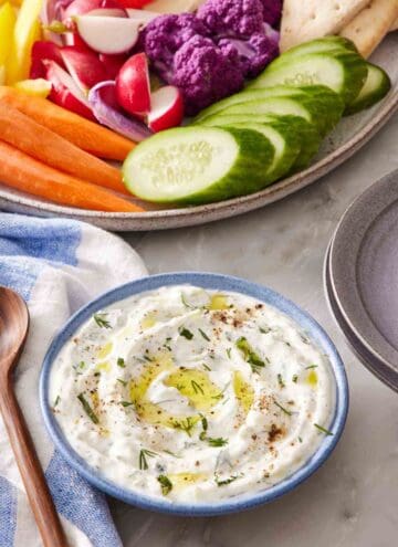 Tzatziki in a small blue bowl with a platter of vegetables half in frame.