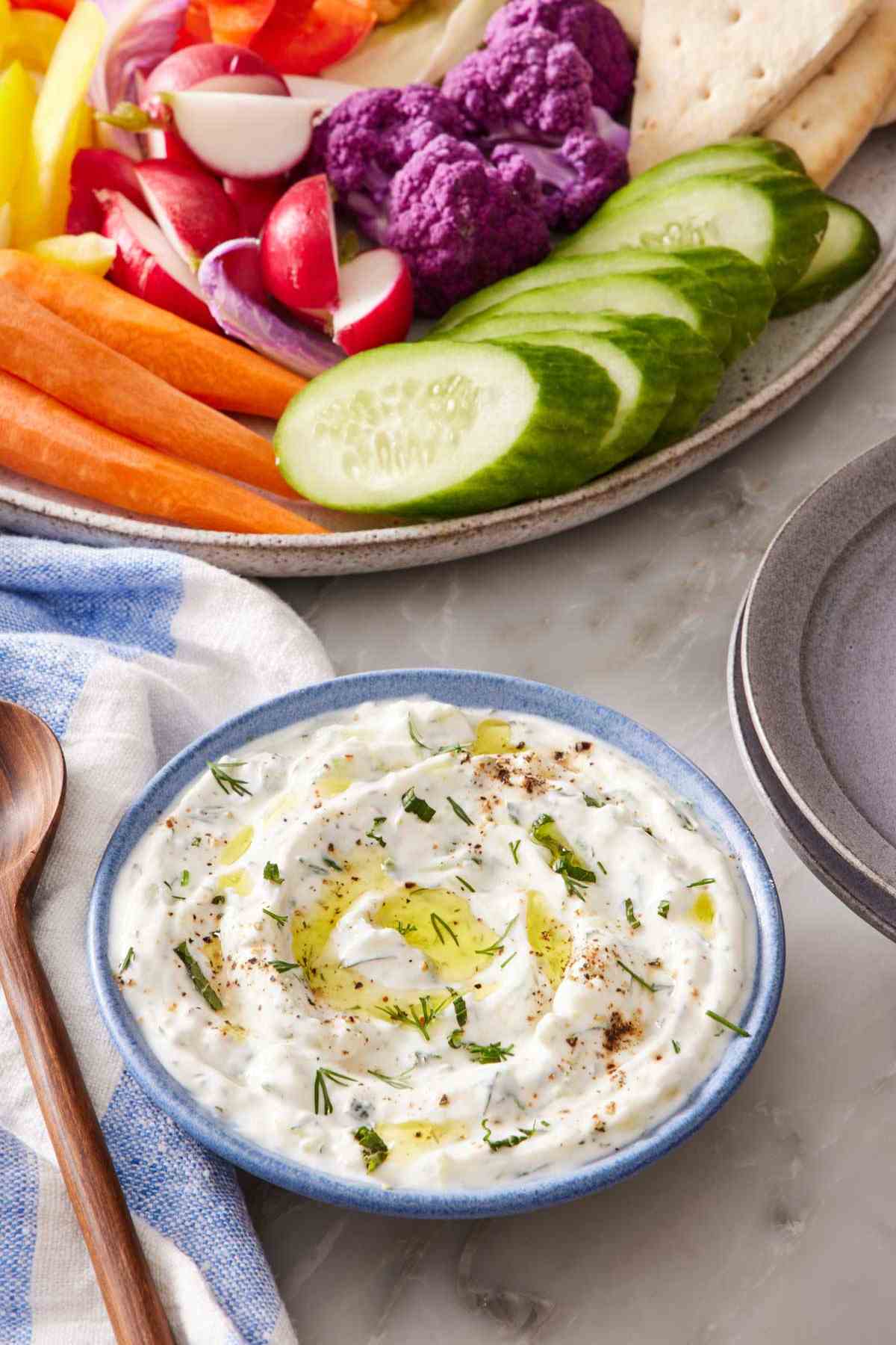 Tzatziki in a small blue bowl with a platter of vegetables half in frame.