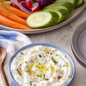 Pinterest graphic showing tzatziki in a small bowl with vegetables on a platter in the background.