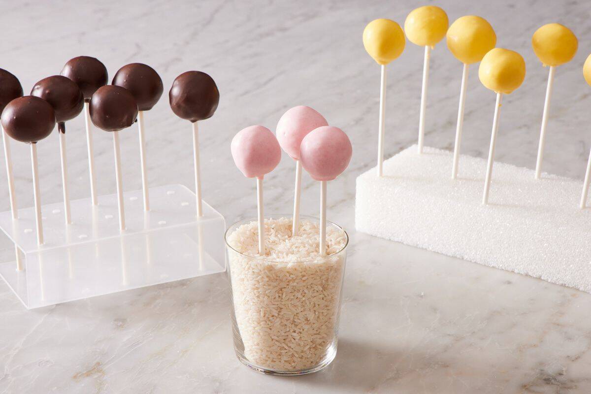 Cake pops in different holders: styrofoam block, a glass of rice, and a plastic cake pop holder.
