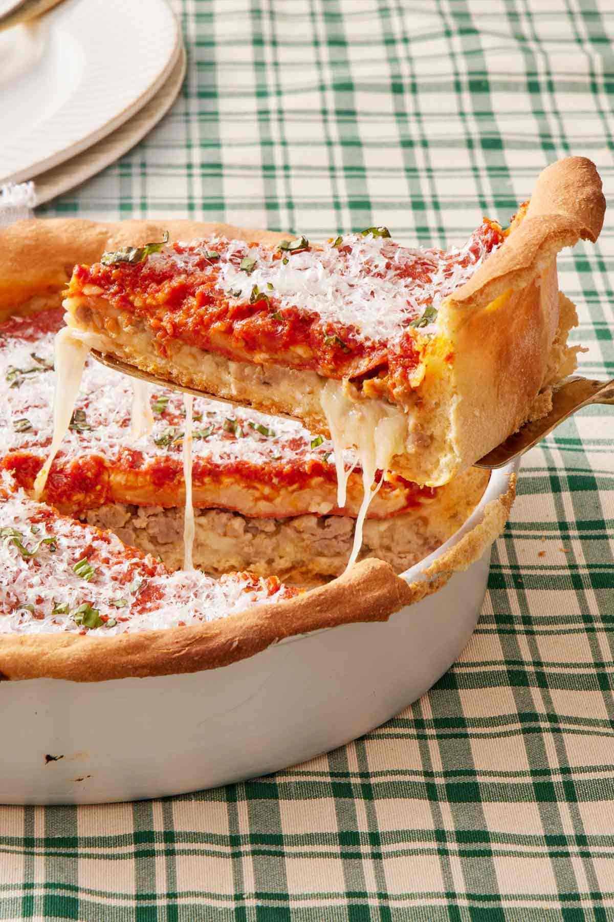 A slice of homemade deep dish pizza lifted out of the dish containing the rest of the pizza.
