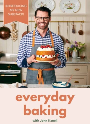 Image of John Kanell in his kitchen holding a cake on a cake plate to launch his new Substack.