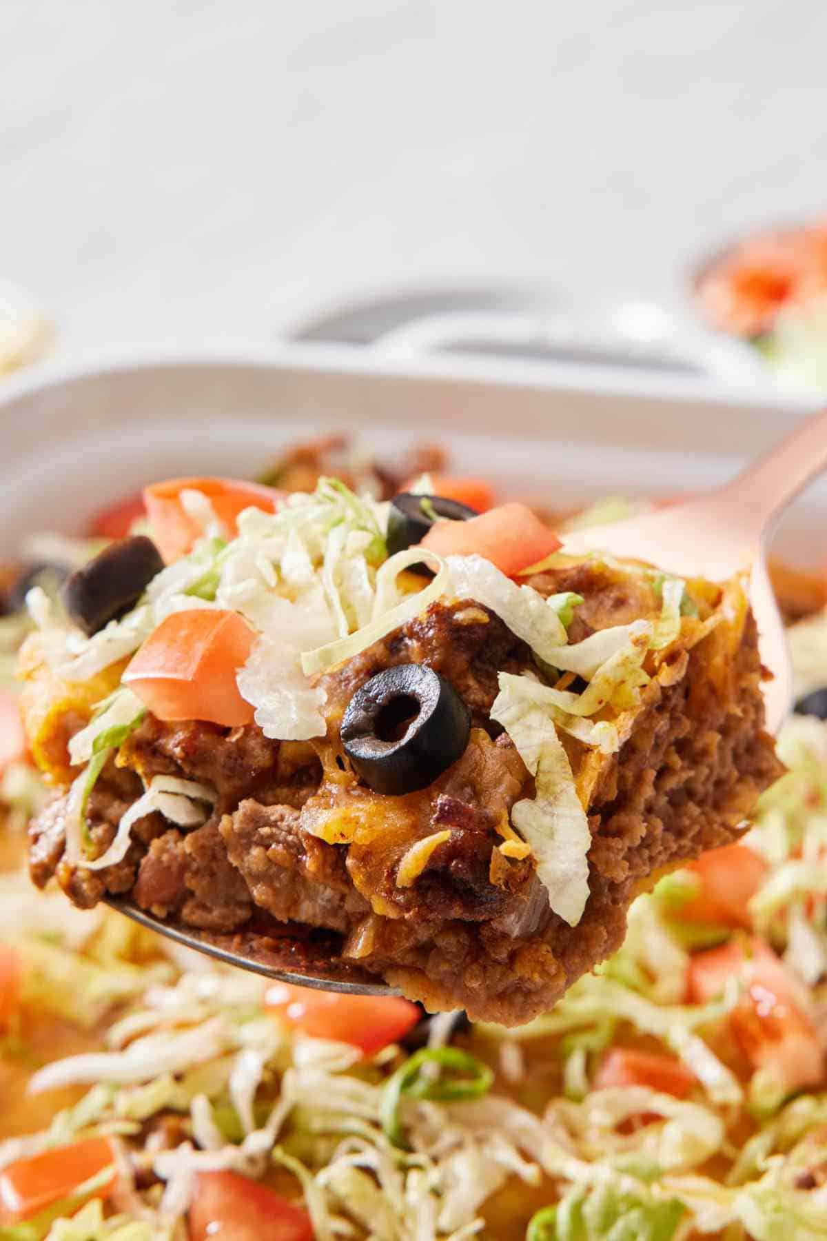 Close up of a serving of taco casserole on a metal spatula with the rest of the casserole out of focus underneath.